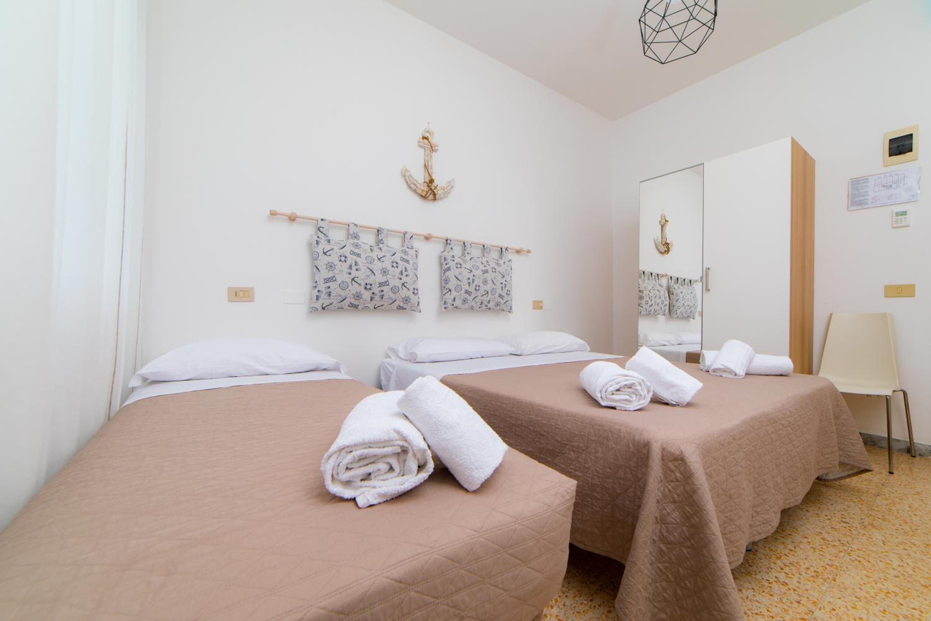 A hotel room with two beds, a mirror, a towel rack, and a chair.