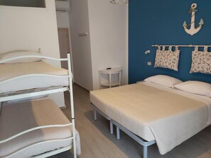 A room with bunk beds, a single bed, a small table, and a wall with nautical decorations. - Hotel 21 (Riccione)