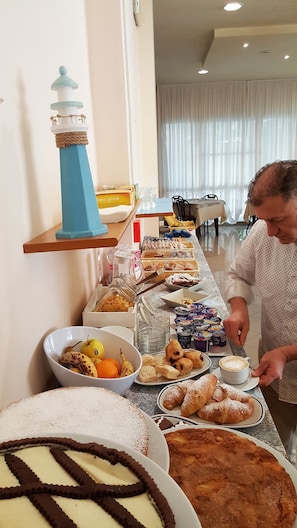 A buffet setup with various food items, a lighthouse decoration, and a person serving coffee. - Hotel 21 (Riccione)