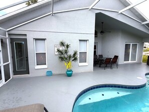 A covered outdoor area with a pool, a dining table with chairs, and a potted plant. - Beautifully Remodeled Pool Home in Southern Dunes (Haines City)