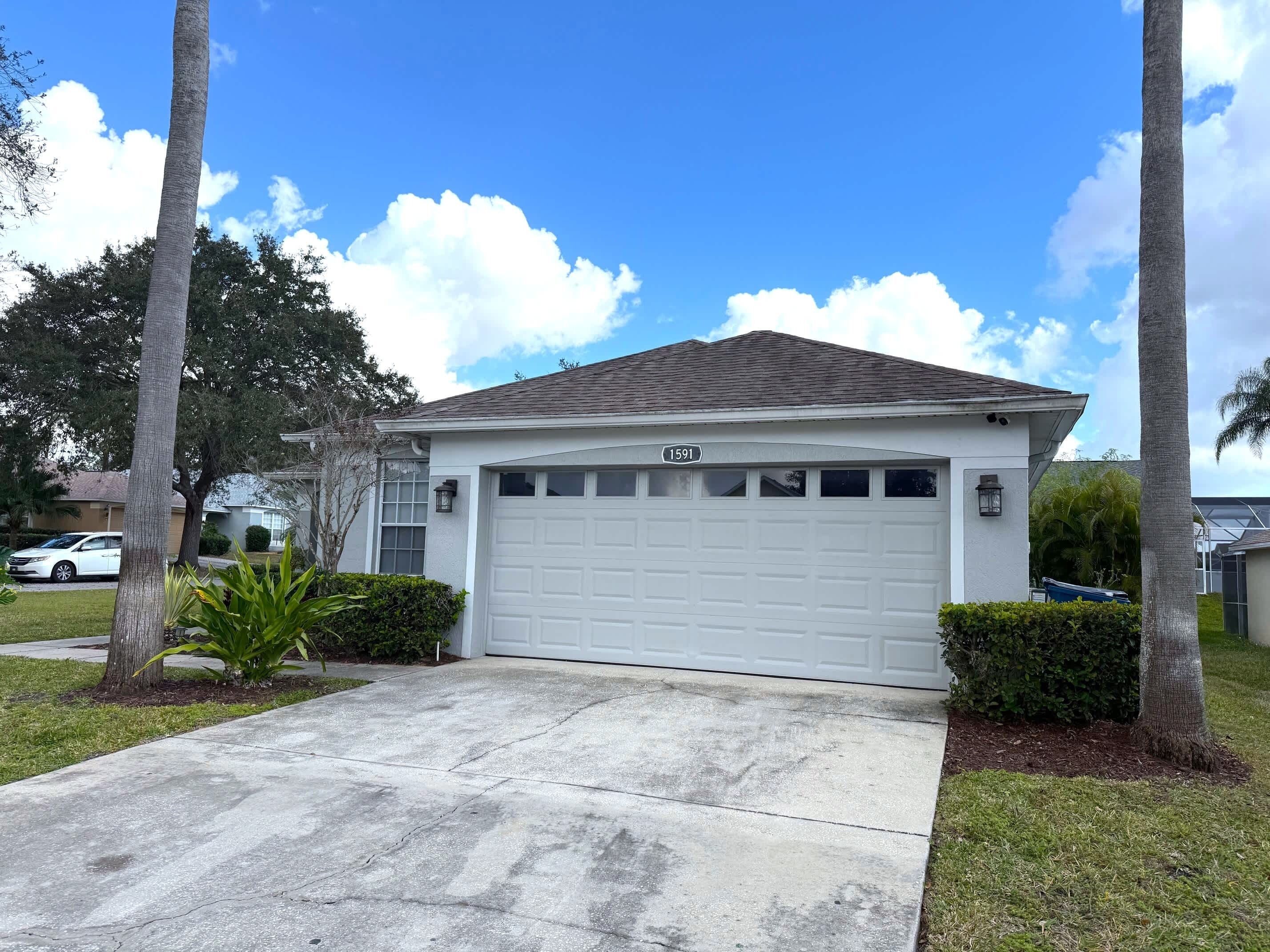 A single-story house with a white garage door, a number '1591' on the garage door, and a clear blue sky with clouds.