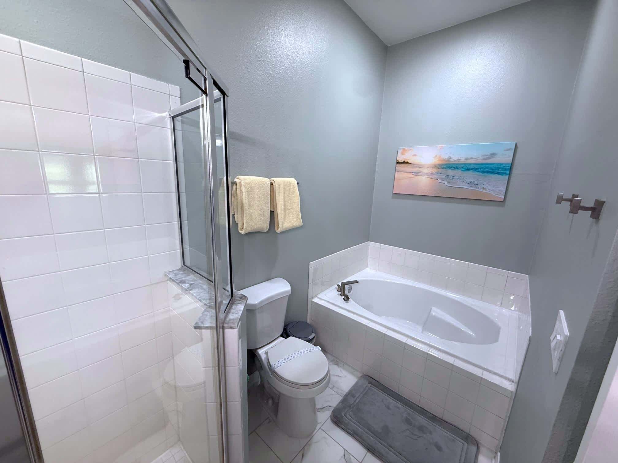Un baño con cabina de ducha de vidrio, un inodoro, una bañera y un cuadro de una playa en la pared.
