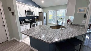 A modern kitchen with granite countertops, stainless steel appliances, and a large island with bar stools. - Beautiful Remodeled Townhome in Southern Dunes (Haines City)