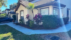 A residential house with a tiled roof, a front yard with various plants, and a sidewalk. - Beautiful Remodeled Townhome in Southern Dunes (Haines City)