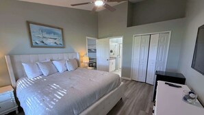 A bedroom with a large bed, a ceiling fan, a painting, a desk, and a wardrobe. - Beautiful Remodeled Townhome in Southern Dunes (Haines City)