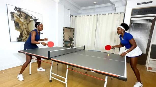 Dues persones jugant a tennis taula en una habitació amb una taula de ping-pong, terres de fusta i un penjador.
