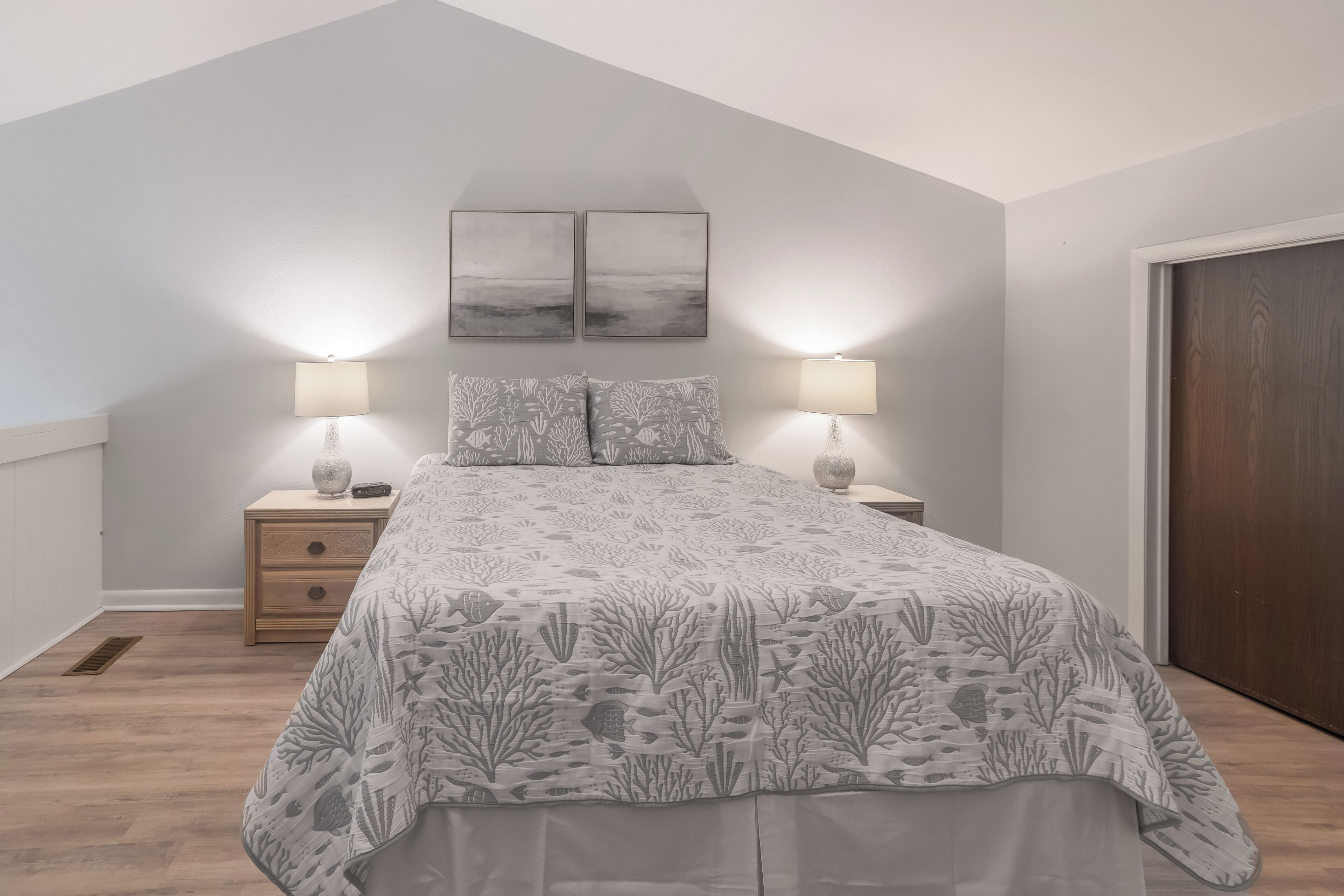 Ein Schlafzimmer mit einem Bett, zwei Nachttischlampen, einem Nachttisch und zwei an der Wand befestigten Bilderrahmen.