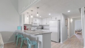 A modern kitchen with white cabinets, a central island, bar stools, and pendant lighting. - Suite + Loft, Pool & Stunning Ocean Views! (Surf City)