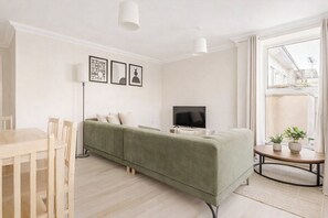 Ein schlicht eingerichtetes Wohnzimmer mit Sofa, Fernseher und Esstisch.