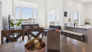 Een ruime woonkamer met een groot raam, een eethoek met een houten tafel, en een keuken met een aanrecht.