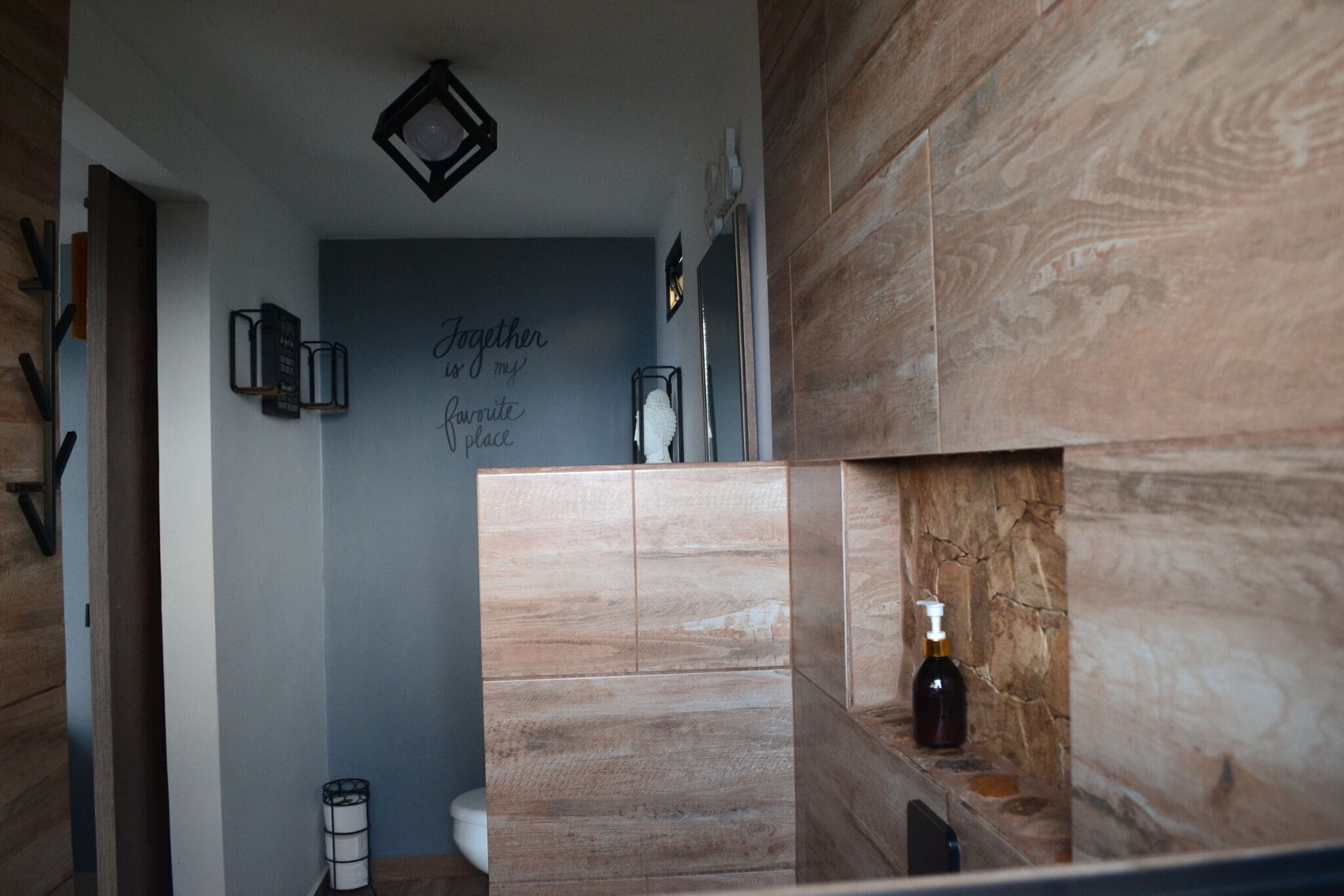 A bathroom with a wooden vanity, a wall-mounted light fixture, and a decorative sign.