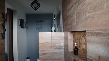 A bathroom with a wooden vanity, a wall-mounted light fixture, and a decorative sign.