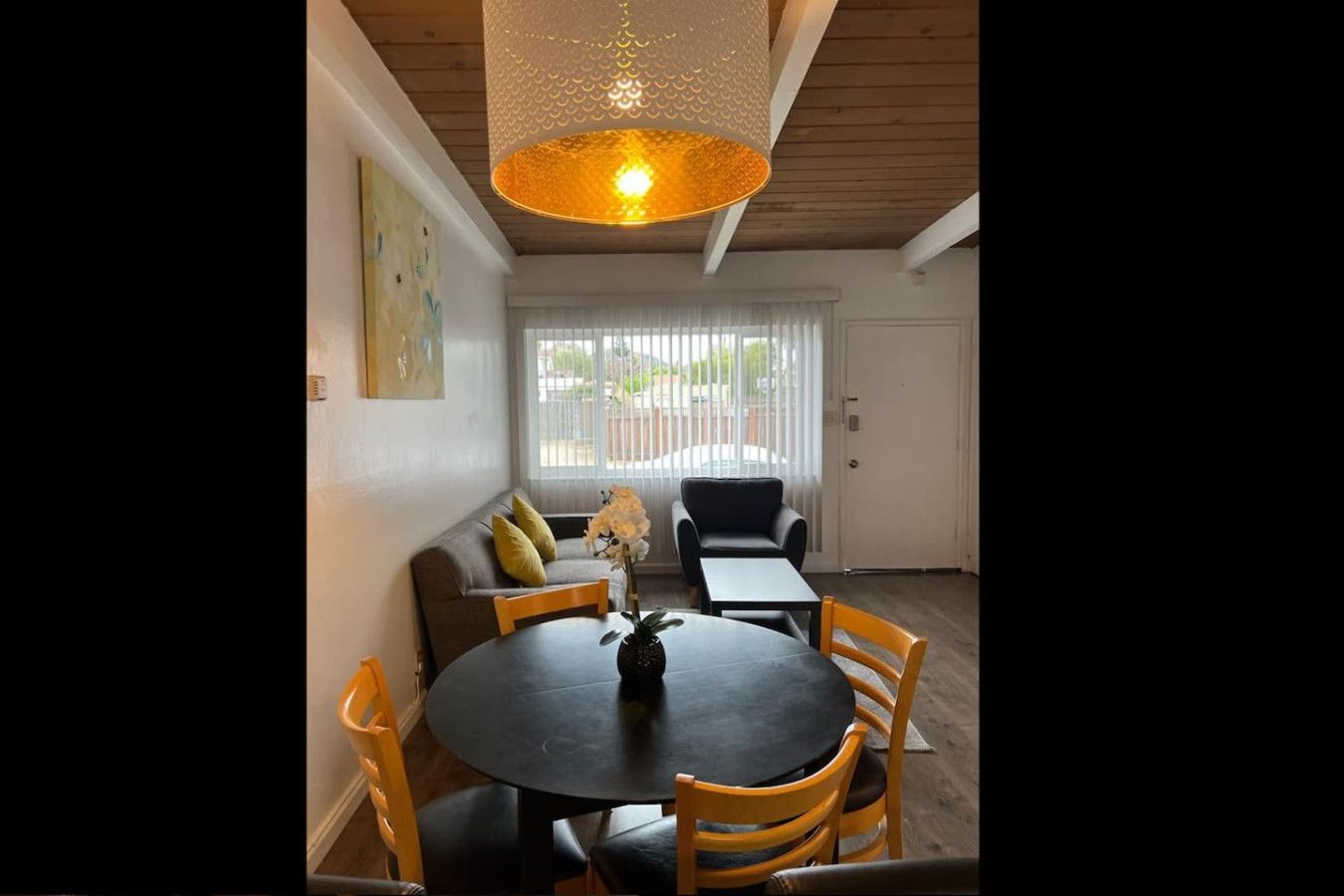 Ein Essbereich mit einem runden Tisch, Stühlen, einer Hängelampe und einer Couch mit Kissen.