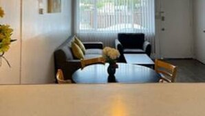 Un comedor con una mesa redonda, sillas, una lámpara colgante y un ventanal con persianas.