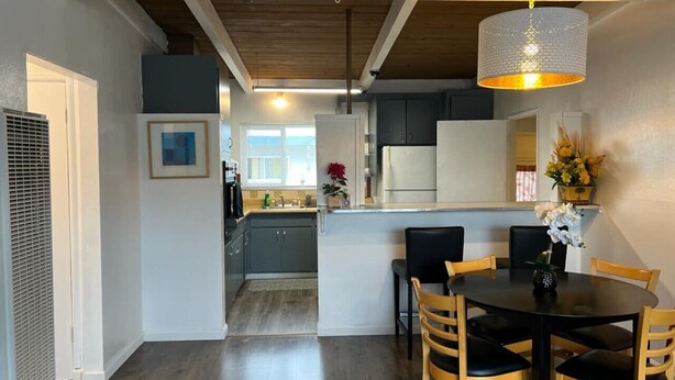 Una cocina moderna con zona de comedor, vigas de techo de madera y una lámpara colgante.