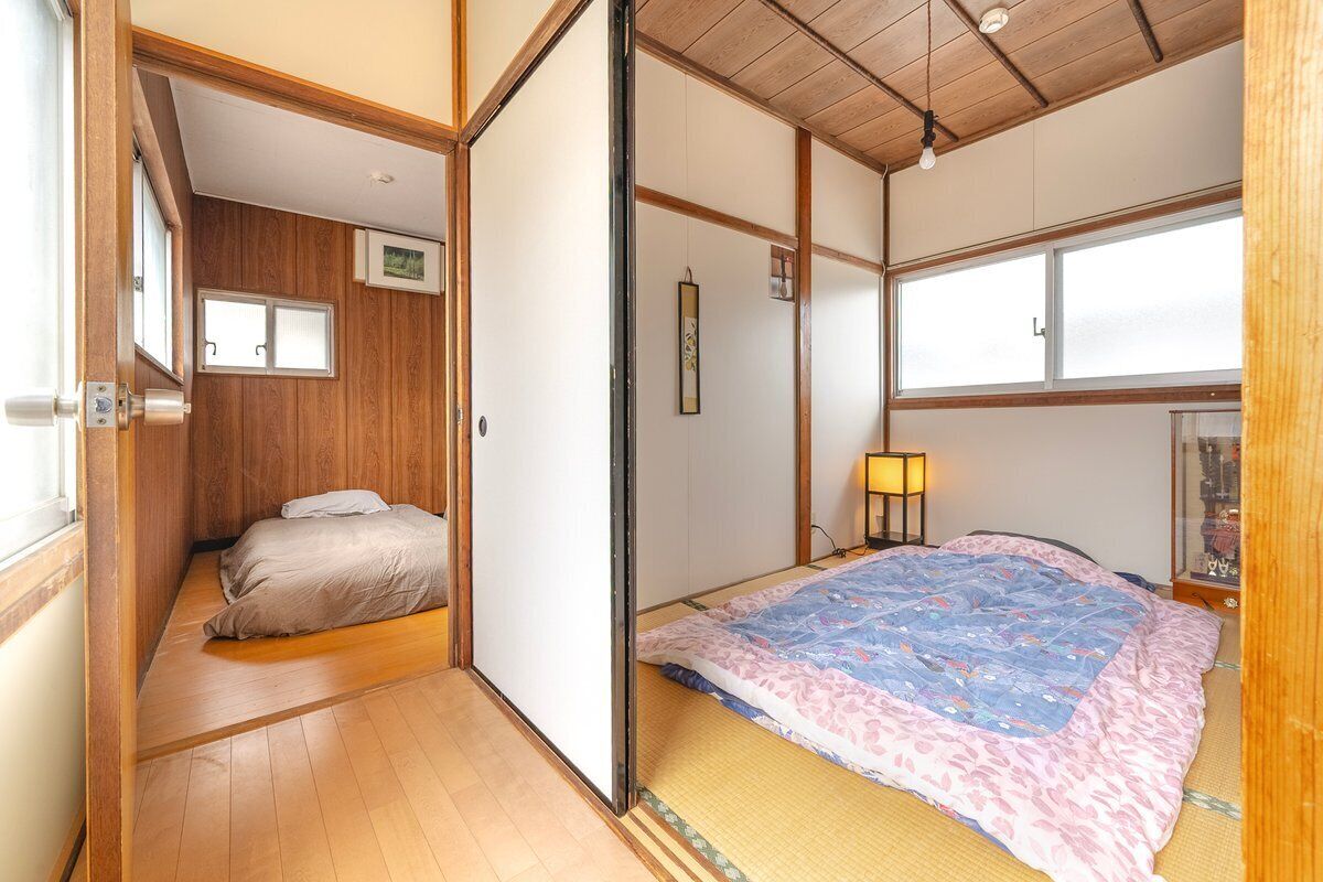 A traditional Japanese room with tatami flooring, a bed with a patterned blanket, a shoji screen door, and a small window.
