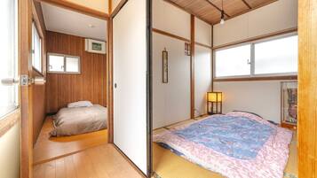 A traditional Japanese room with tatami flooring, a bed with a patterned blanket, a shoji screen door, and a small window.