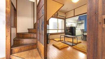 A traditional Japanese interior with a wooden staircase, tatami mats, a kitchen area, and a dining space.