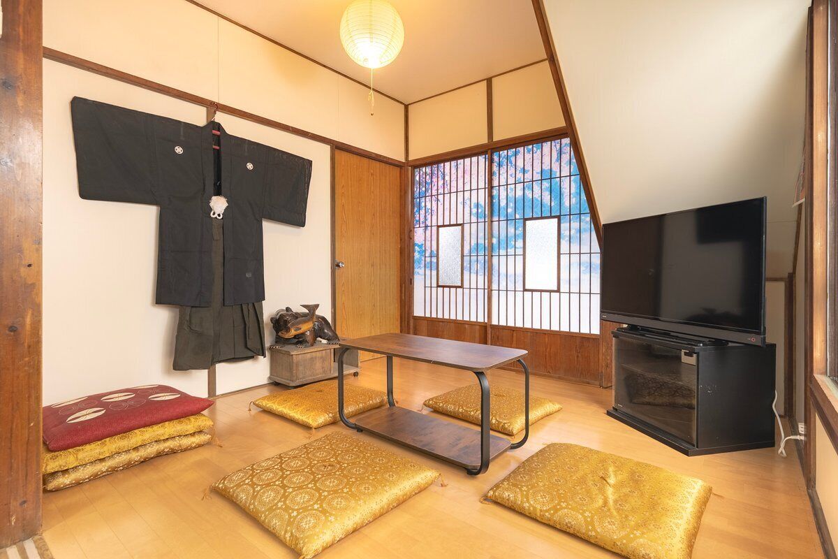 A traditional Japanese room with tatami flooring, a television, a low table, and a sliding door with a view.
