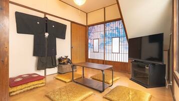 A traditional Japanese room with tatami flooring, a television, a low table, and a sliding door with a view.