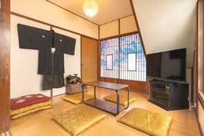 Ein traditioneller japanischer Raum mit Tatami-Boden, einem Fernseher, einem niedrigen Tisch und einer Schiebetür mit Blick.