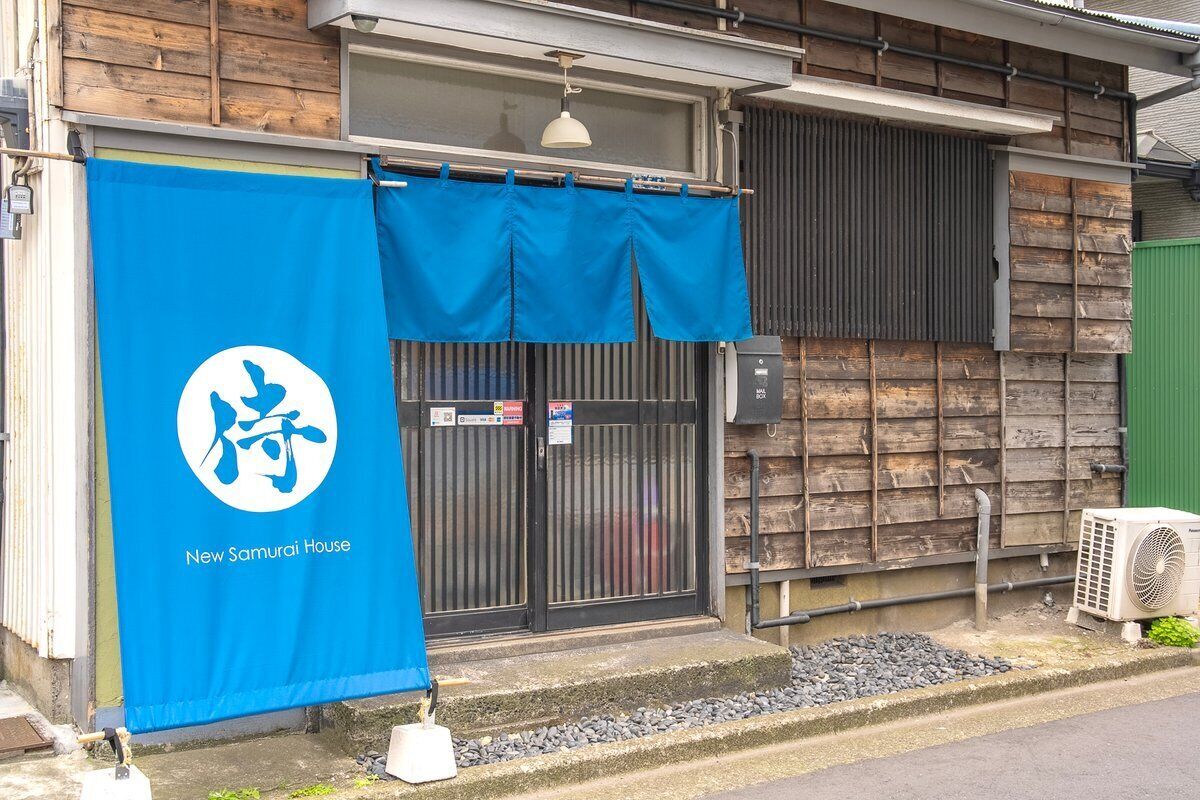 A building with a blue banner featuring a logo and text, a black gate, and an air conditioning unit outside.