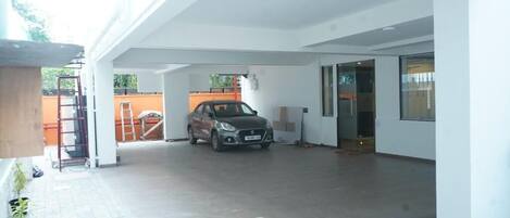 A spacious indoor parking area with a car parked in the center, a ladder, and a potted plant on the left.