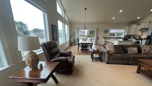 Ein geräumiges Wohnzimmer mit Ledersessel, Sofa, Esstisch und einer Küche im Hintergrund.