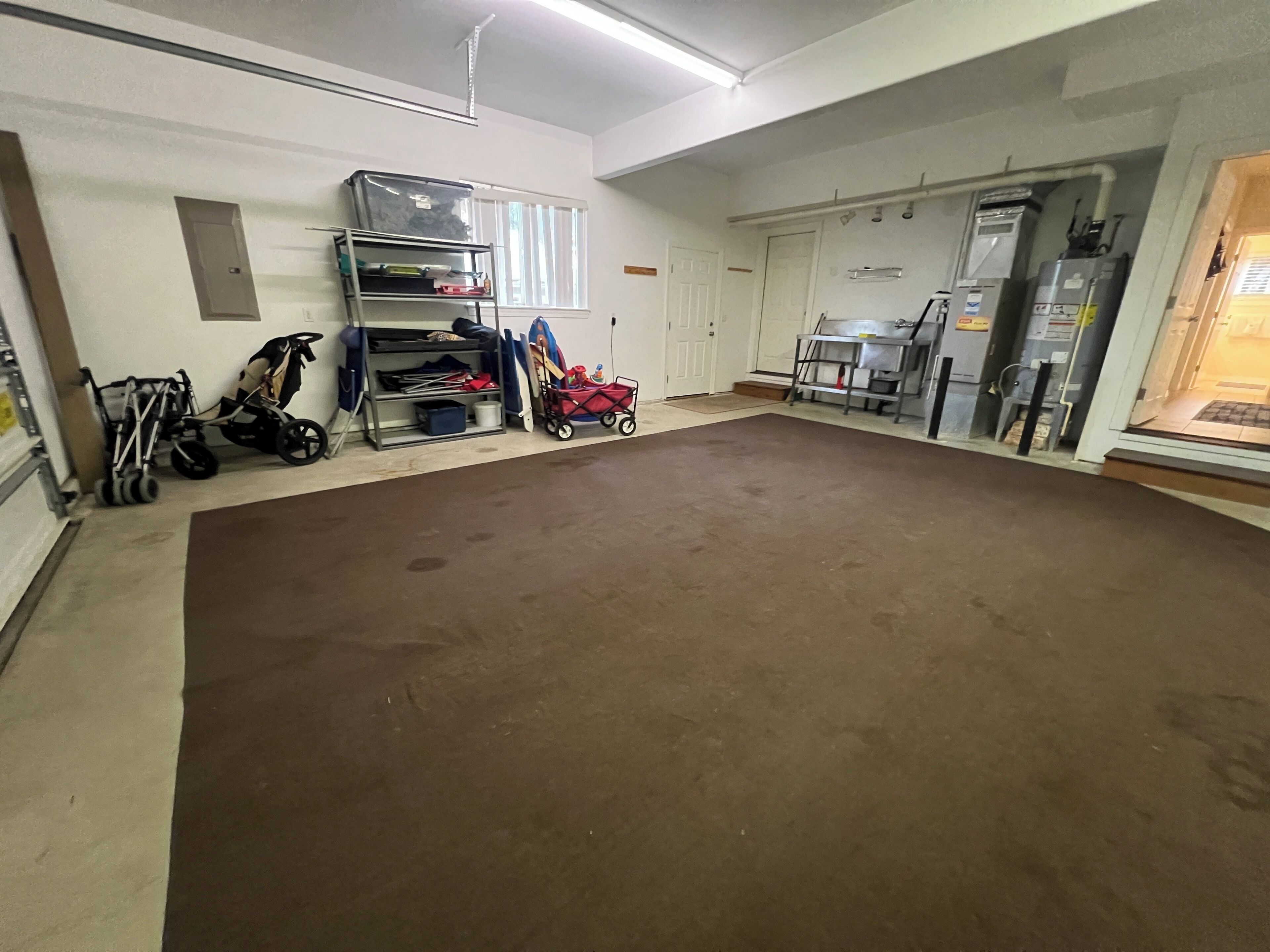 A spacious room with a large brown floor, a metal shelving unit with various items, a stroller, and a red toy car.