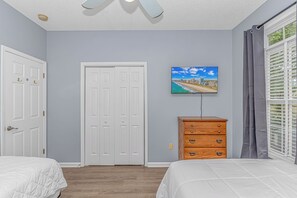 A bedroom with two beds, a wooden dresser, a white door, and a wall-mounted TV. - The Coastal Catch Ground-Floor Oasis near Beach, Pool & Golf (Little River)