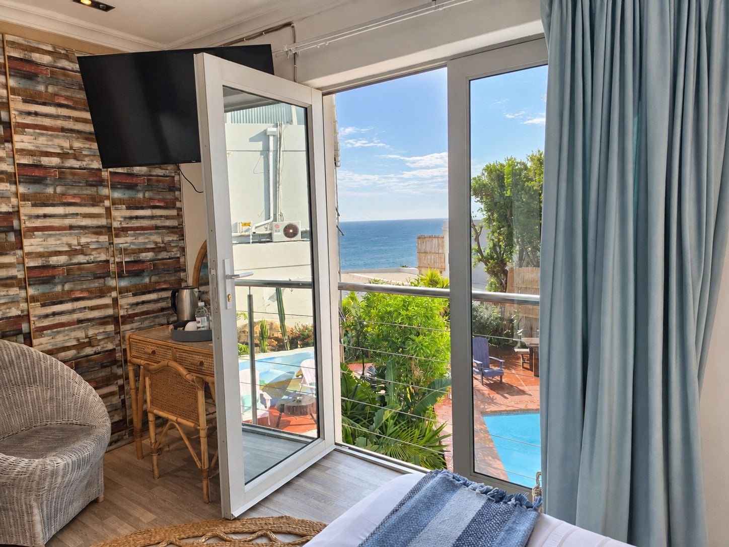 Una habitación con un gran ventanal corredero que da a un balcón con piscina y vista al océano.