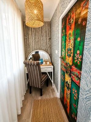 Ein Zimmer mit einem Streifenstuhl, einem kleinen Tisch mit Tablett, einer gewebten Hängelampe und einer farbenfrohen Tür.