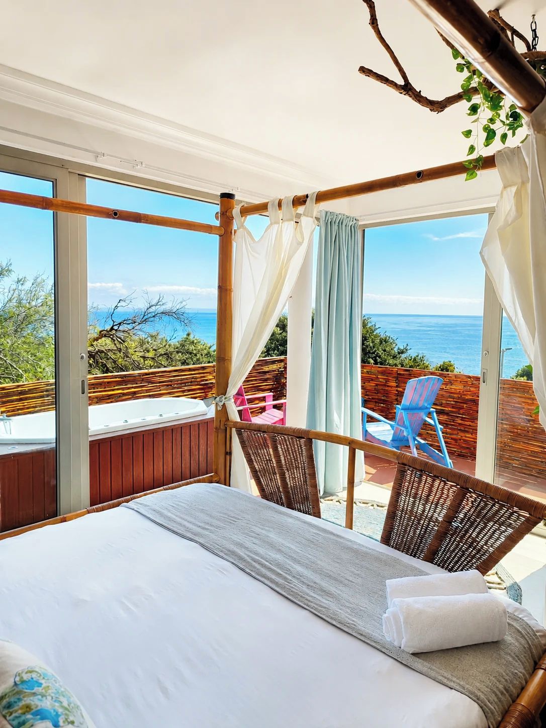 Ein Schlafzimmer mit einem großen Bett, Meerblick und einem Balkon mit Stühlen.
