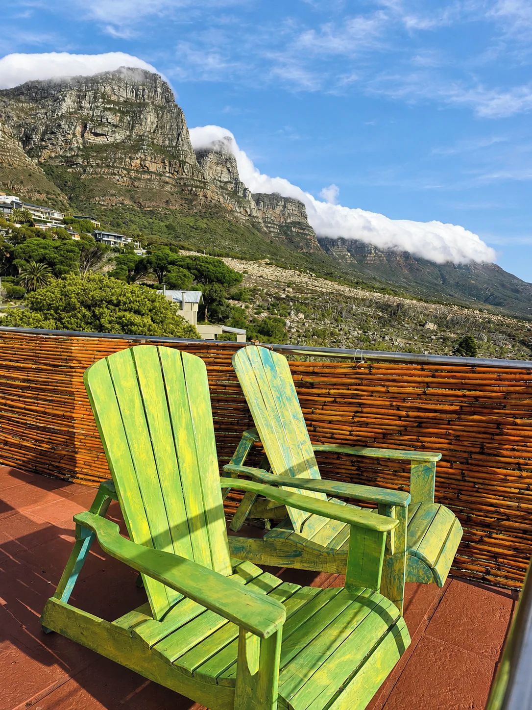 A terrace with green Adirondack chairs, a bamboo fence, and a mountain view.