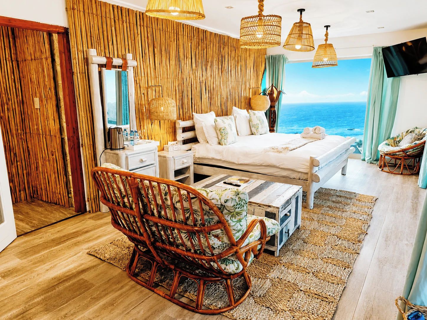 Un dormitorio con cama, mesitas de noche, una silla de mimbre y vista al océano.