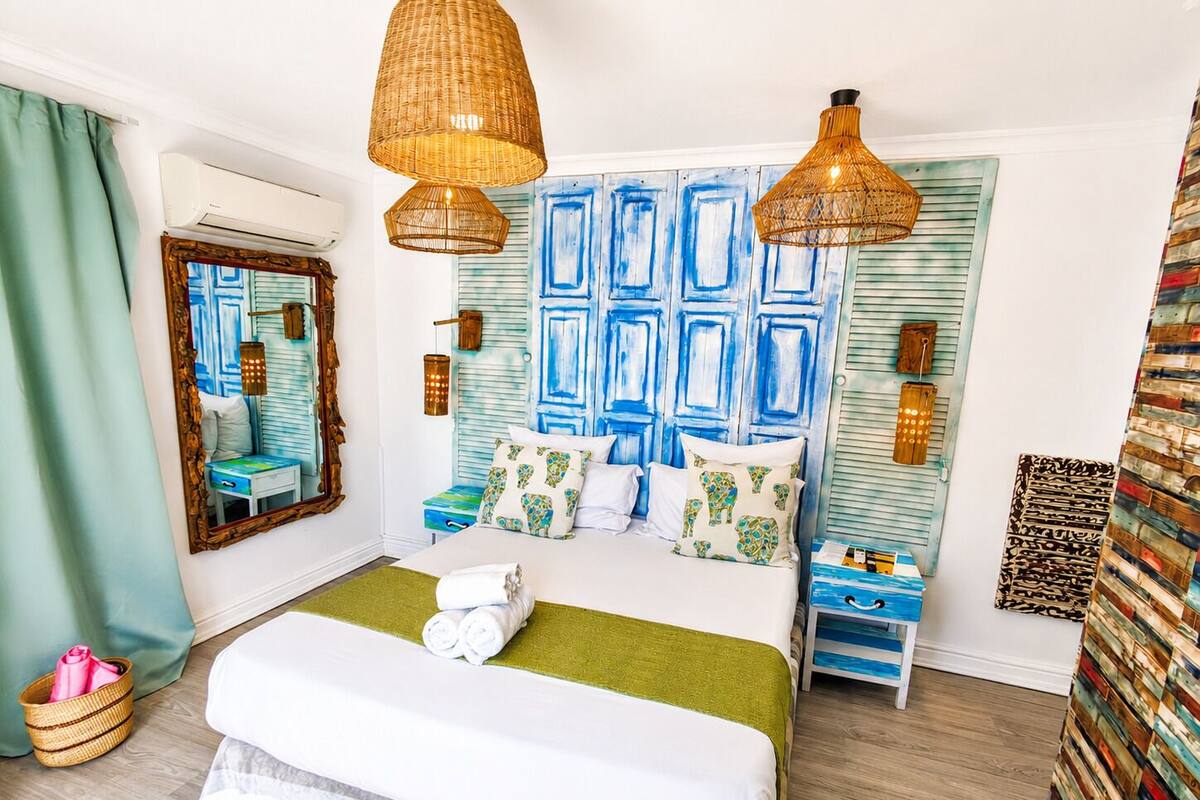 Un dormitorio con cama, mesitas de noche, un espejo y una pared con paneles azules.