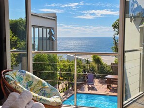Varanda com vista para o mar, piscina e uma cadeira.