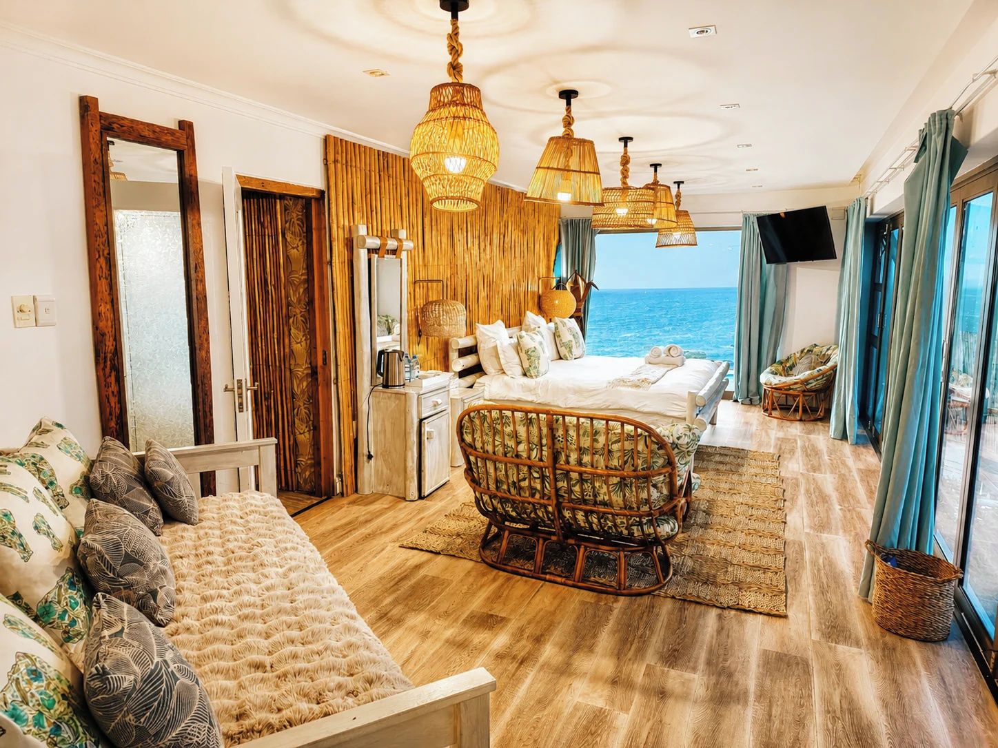A bedroom with a bed, a sofa, a chair, a desk, and a view of the sea.