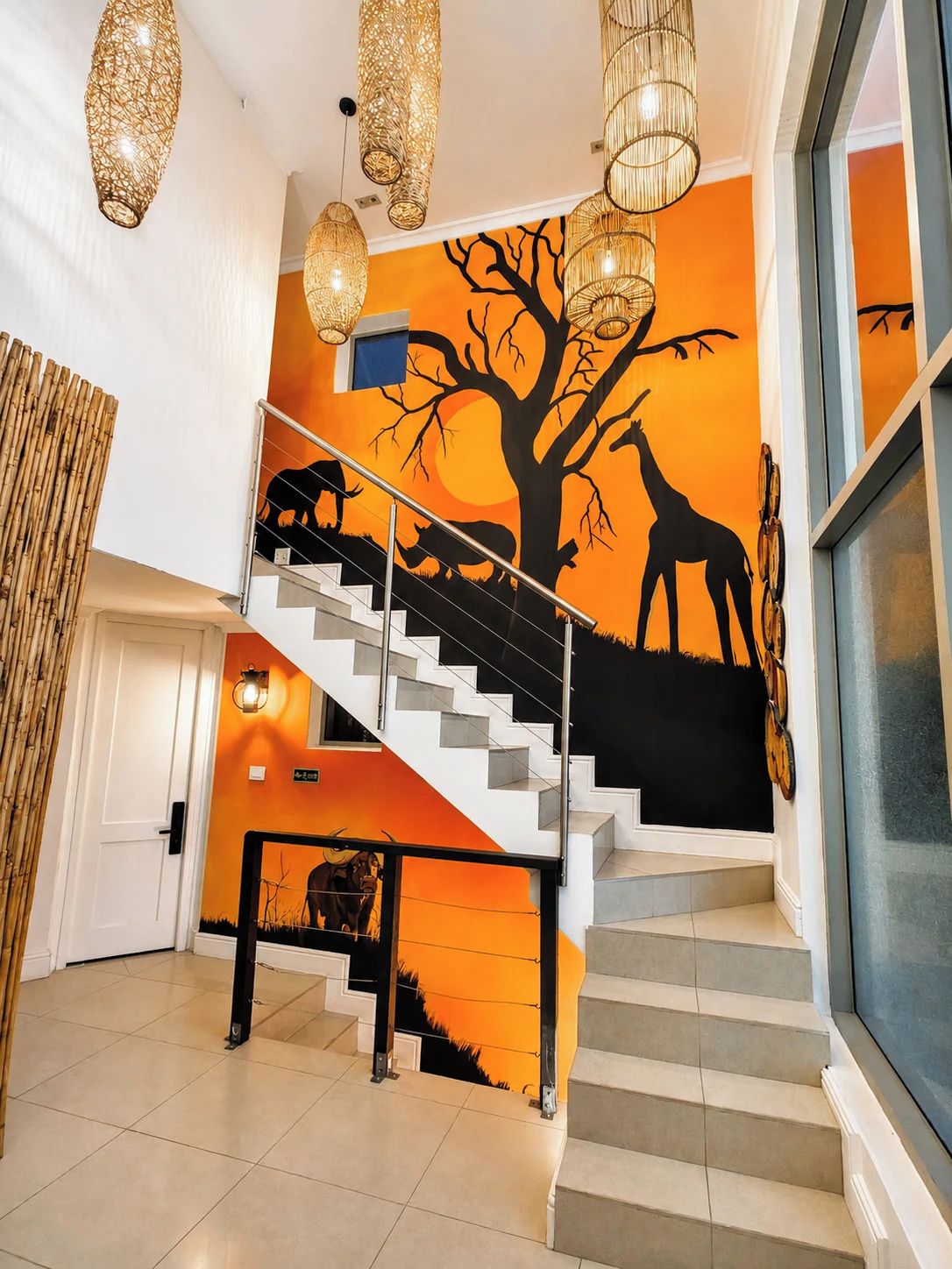 Escadaria com mural de animais e árvore, levando a um quarto com uma grande janela.