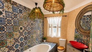 Un baño con una bañera independiente, inodoro, lavamanos de color rojo y espejo.