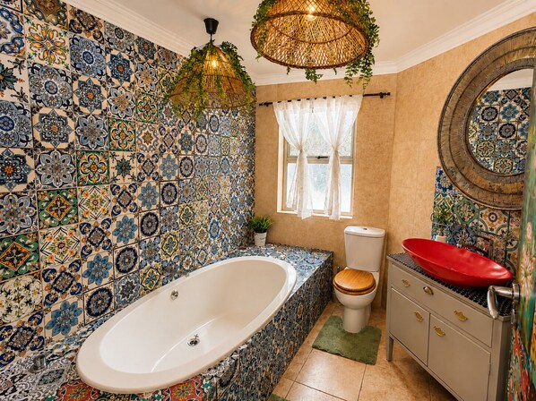Un baño con una bañera independiente, inodoro, lavamanos de color rojo y espejo.