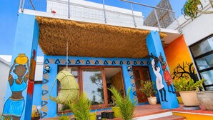 Un edificio con paredes de azul y naranja vibrantes, techo de paja y arte que representa figuras africanas.