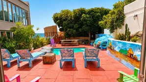 Un área de piscina con sillones de descanso, una mesa de madera y un mural en la pared.
