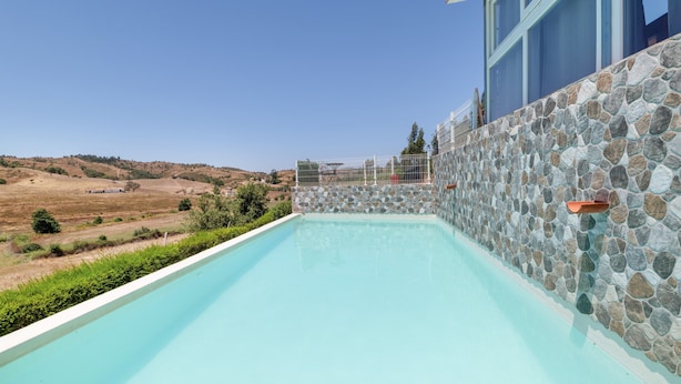 A swimming pool with a stone wall, a clear sky, and a hilly landscape in the background.