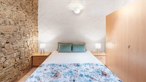 Ein Schlafzimmer mit einer Steinwand, einem Holzschrank, einem Bett mit Blumenmuster-Bettwäsche und Nachttischlampen.