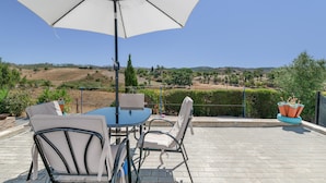 Eine Terrasse im Freien mit Tisch und Stühlen, einem großen Sonnenschirm und Blick auf die Landschaft.