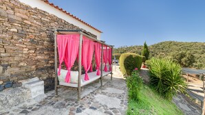 Un edificio de piedra con techo de tejas rojas, un muro de piedra y una cama con cortinas rosas.