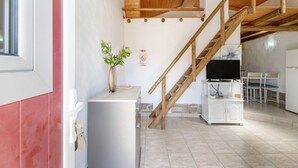 Una habitación con escalera de madera, un armario blanco, un televisor y una planta.