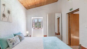 Un dormitorio con cama, almohadas, una ventana, una puerta de madera y una obra de arte colgada en la pared.