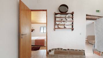 A room with a wooden door, a bed with a pink bedspread, a wall-mounted plate rack, and a stone accent wall.